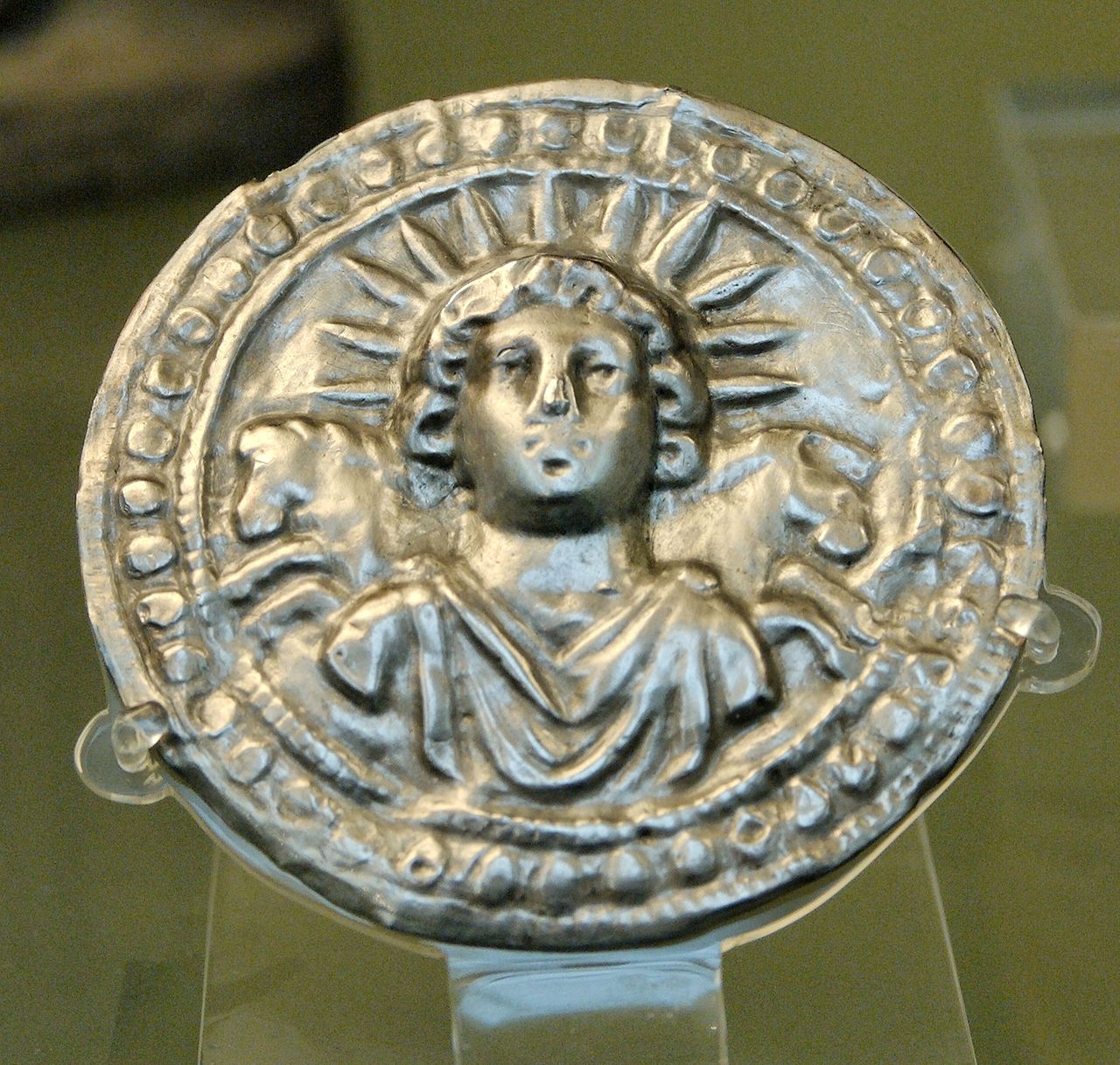 A shiny silver plate showing a glowing sun from ancient Rome.
