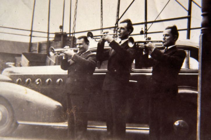 Three trumpet players blowing their horns together in an old photo.