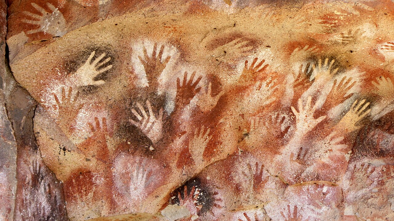 Cave wall covered in colorful handprints from long ago.