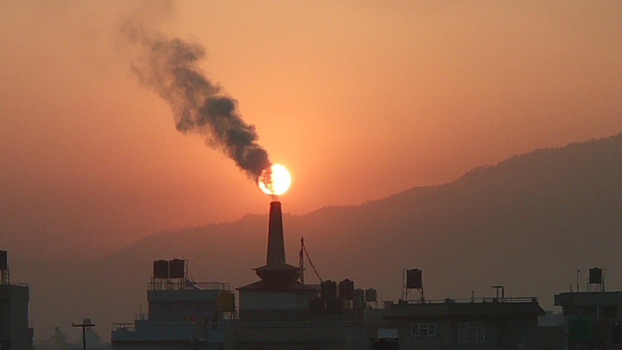 Smoke from a tall factory chimney hides the sun in the sky.