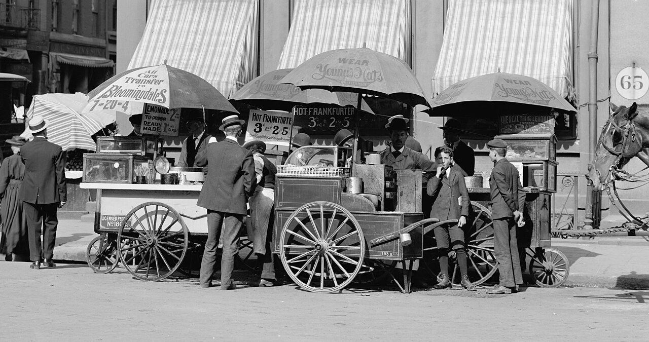 An old photo of hot dog carts on a busy city street.