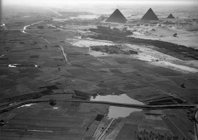 The huge pyramids rise above the sandy desert near green fields.