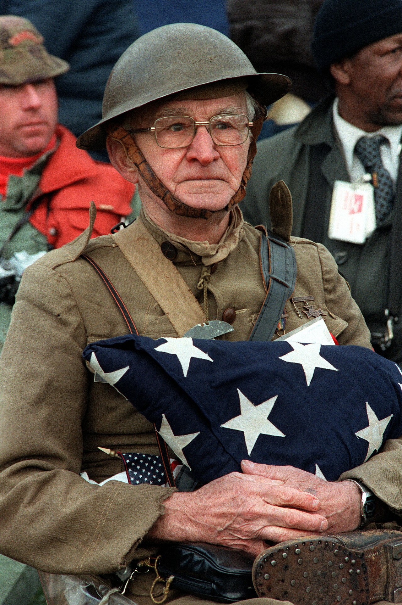 An older veteran proudly holds an American flag at a parade.