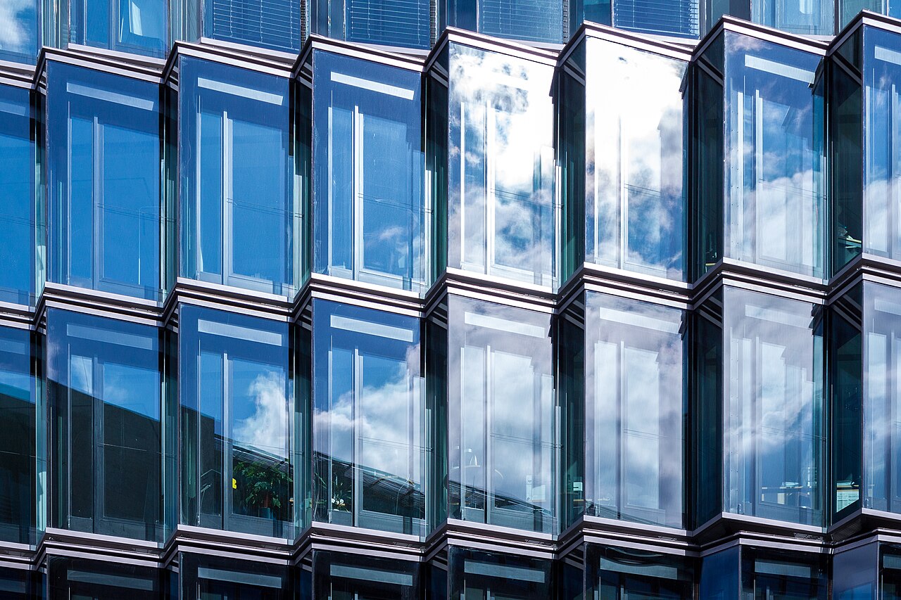 A tall building with a shiny wall made of glass.