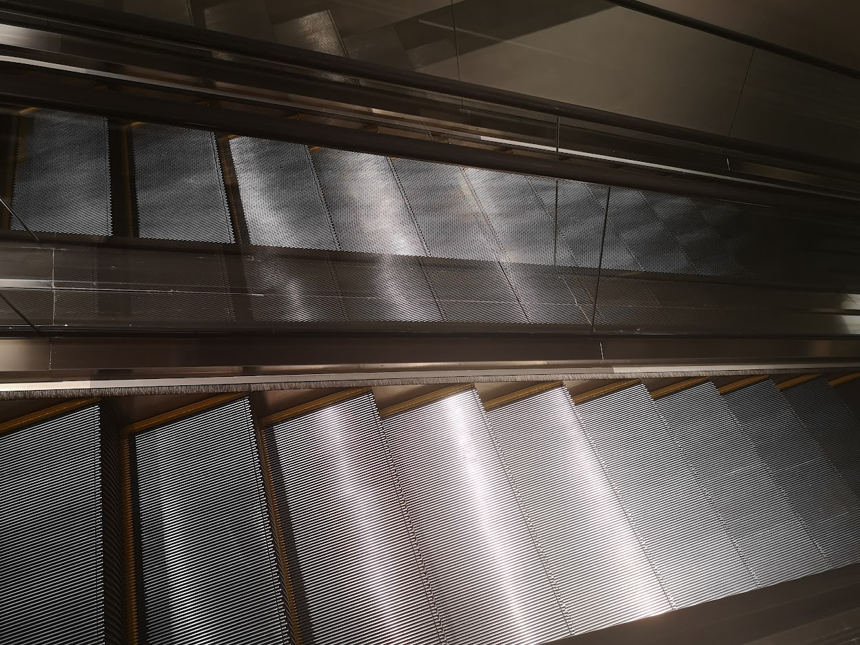 Rows of shiny escalators inside a big, busy mall.