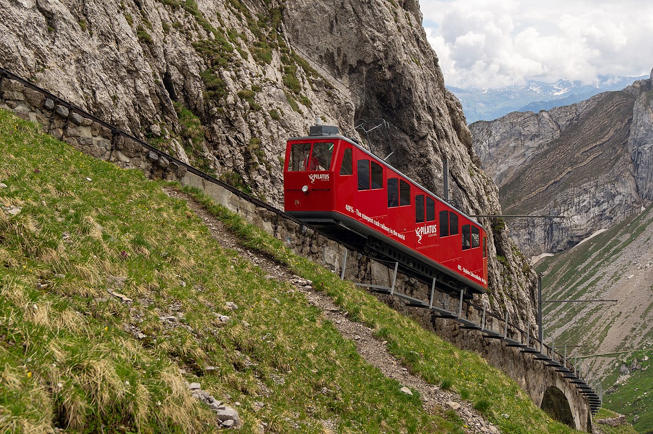A little train climbing up a steep, green mountain.