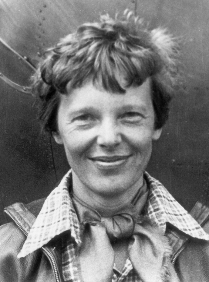 Amelia Earhart standing beneath the nose of her airplane in 1937.