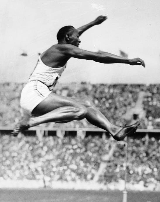 Jesse Owens flying through the air during a long jump at the 1936 Olympics.