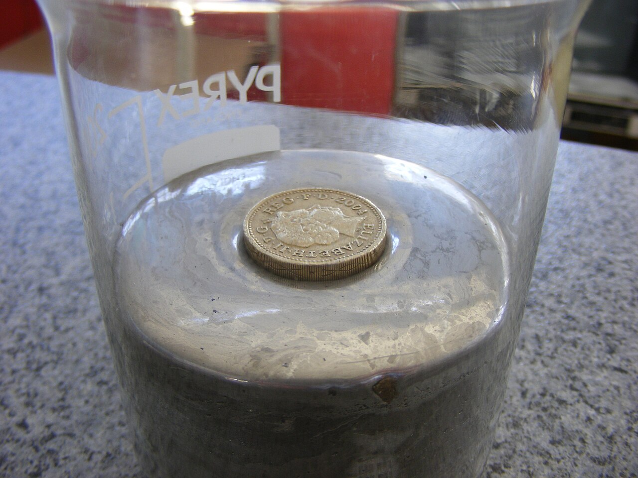 A shiny coin floats on top of a silvery liquid metal.