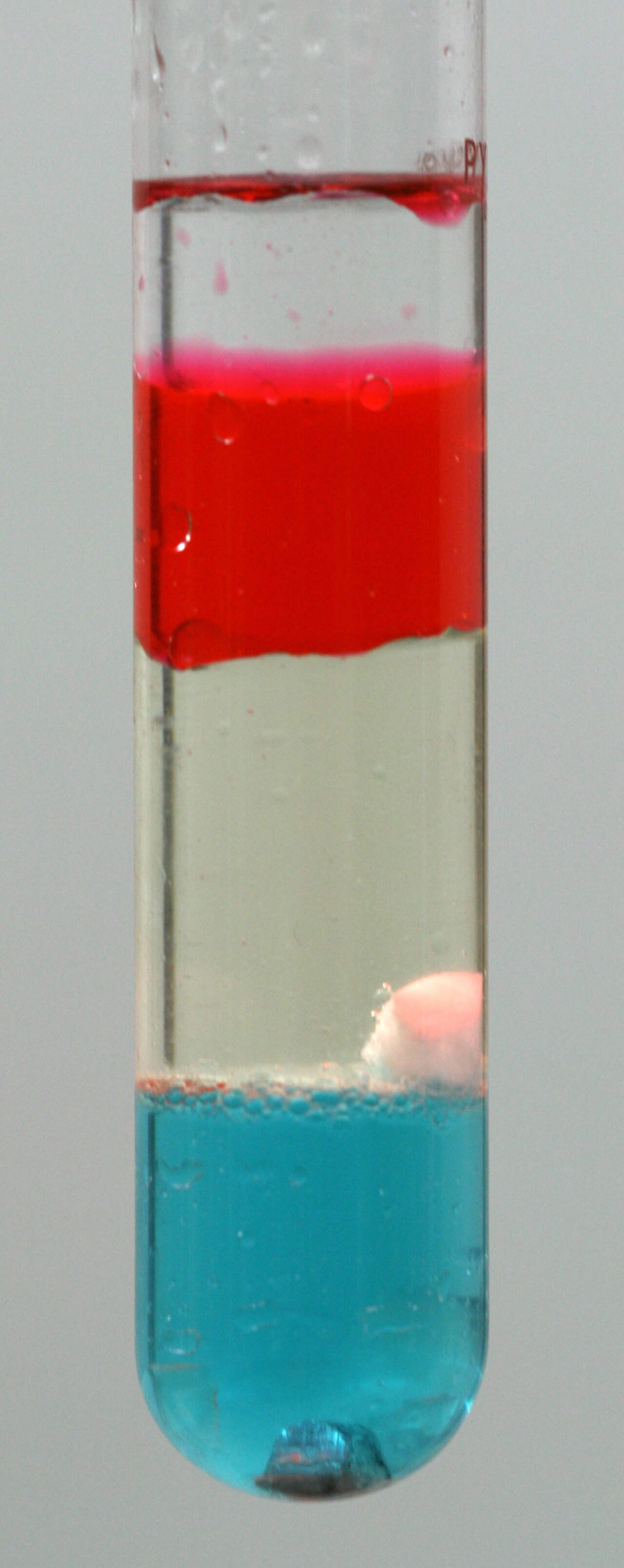 A tall jar with colorful liquids and solids stacked in layers.