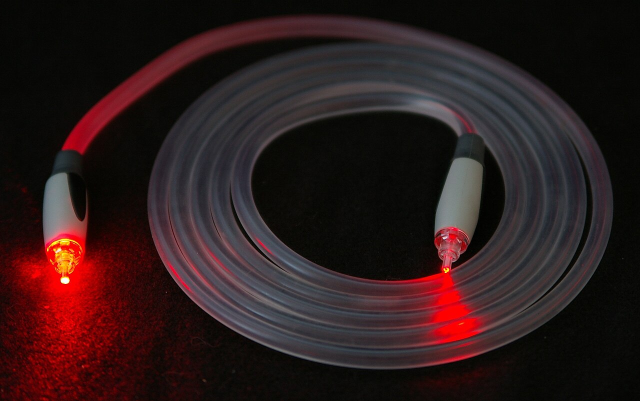 Red laser light shines through a clear fiber optic cable.