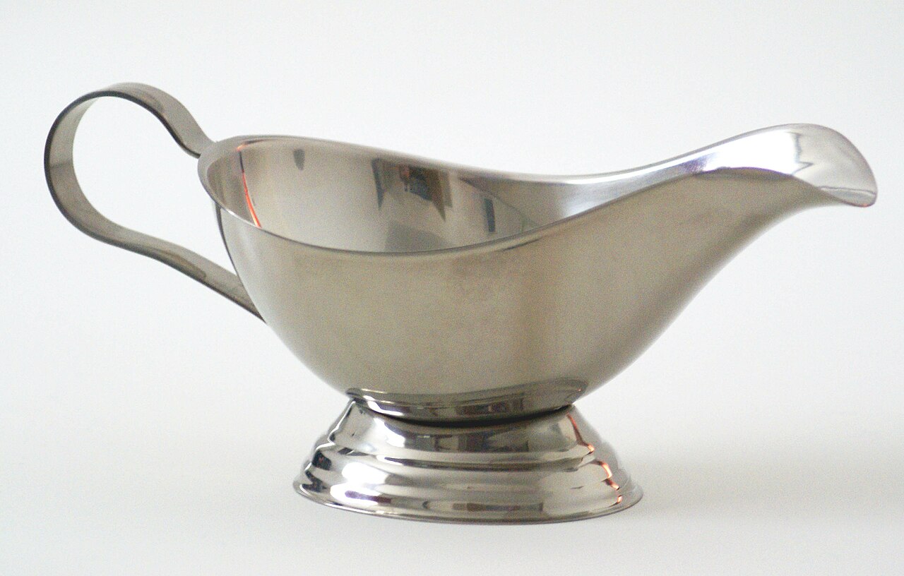 A shiny silver metal gravy boat used at the dinner table.