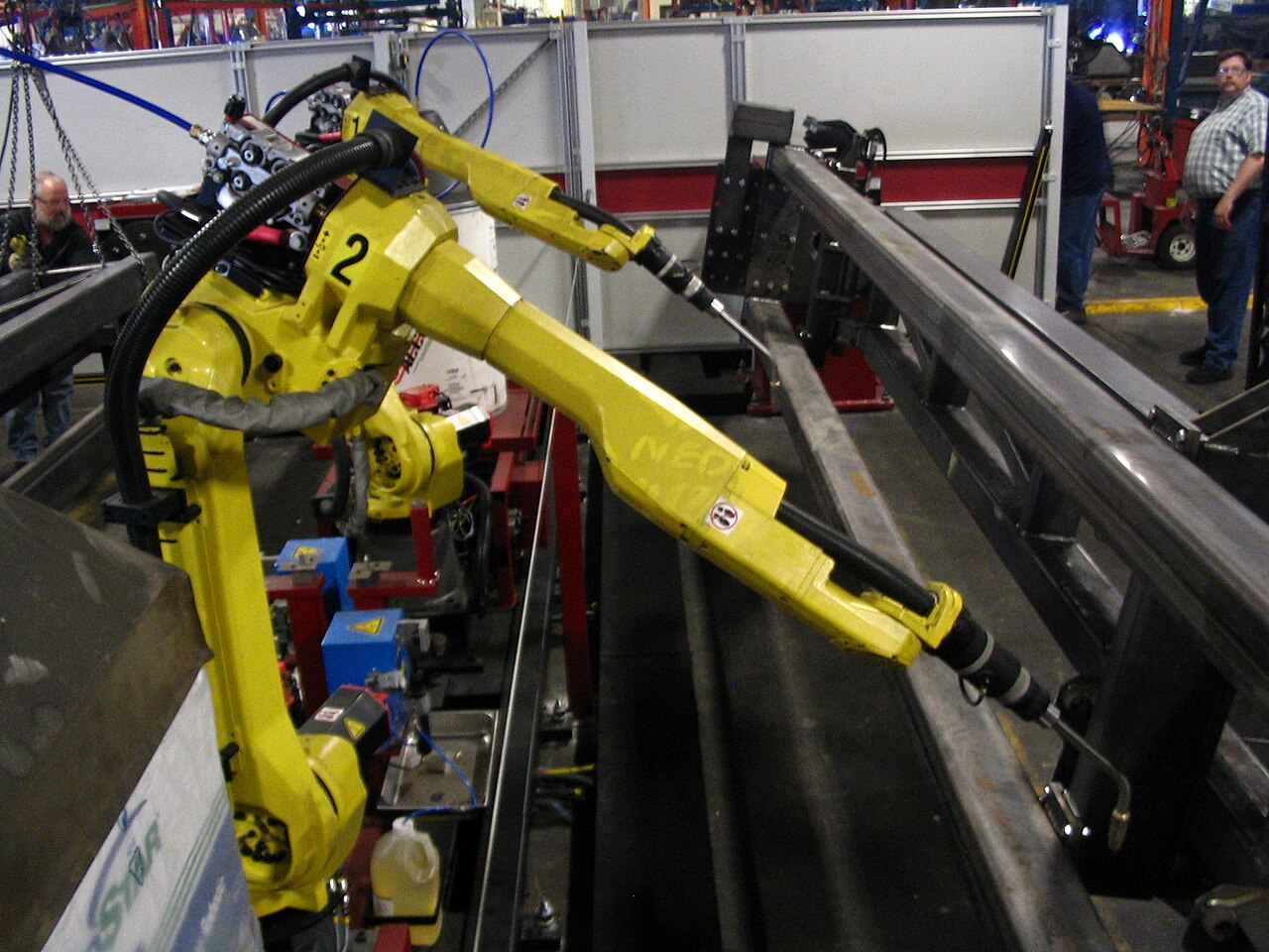 A yellow robot arm welds parts inside a factory.