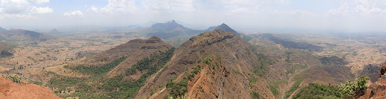 A wide dry-season view from a hilltop with winding train tracks.