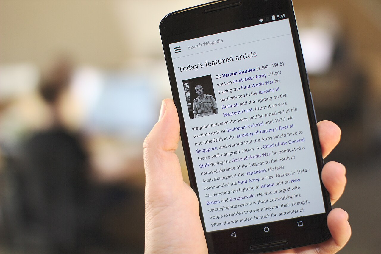 A hand holds a smartphone showing a website on the screen.