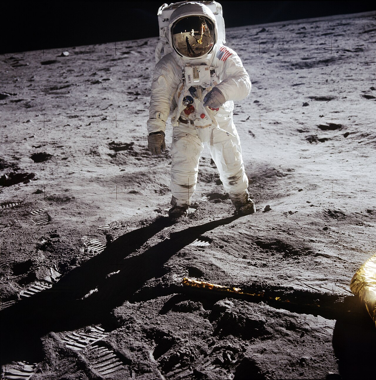 An Apollo 11 astronaut stands on the Moon in his white spacesuit.
