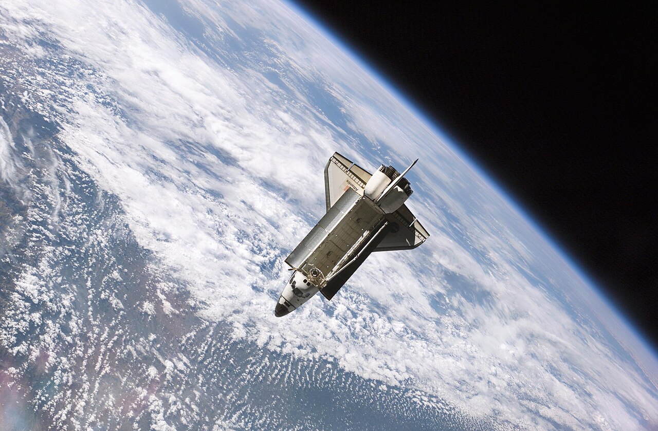 The Space Shuttle Atlantis flies above Earth's swirling white clouds.
