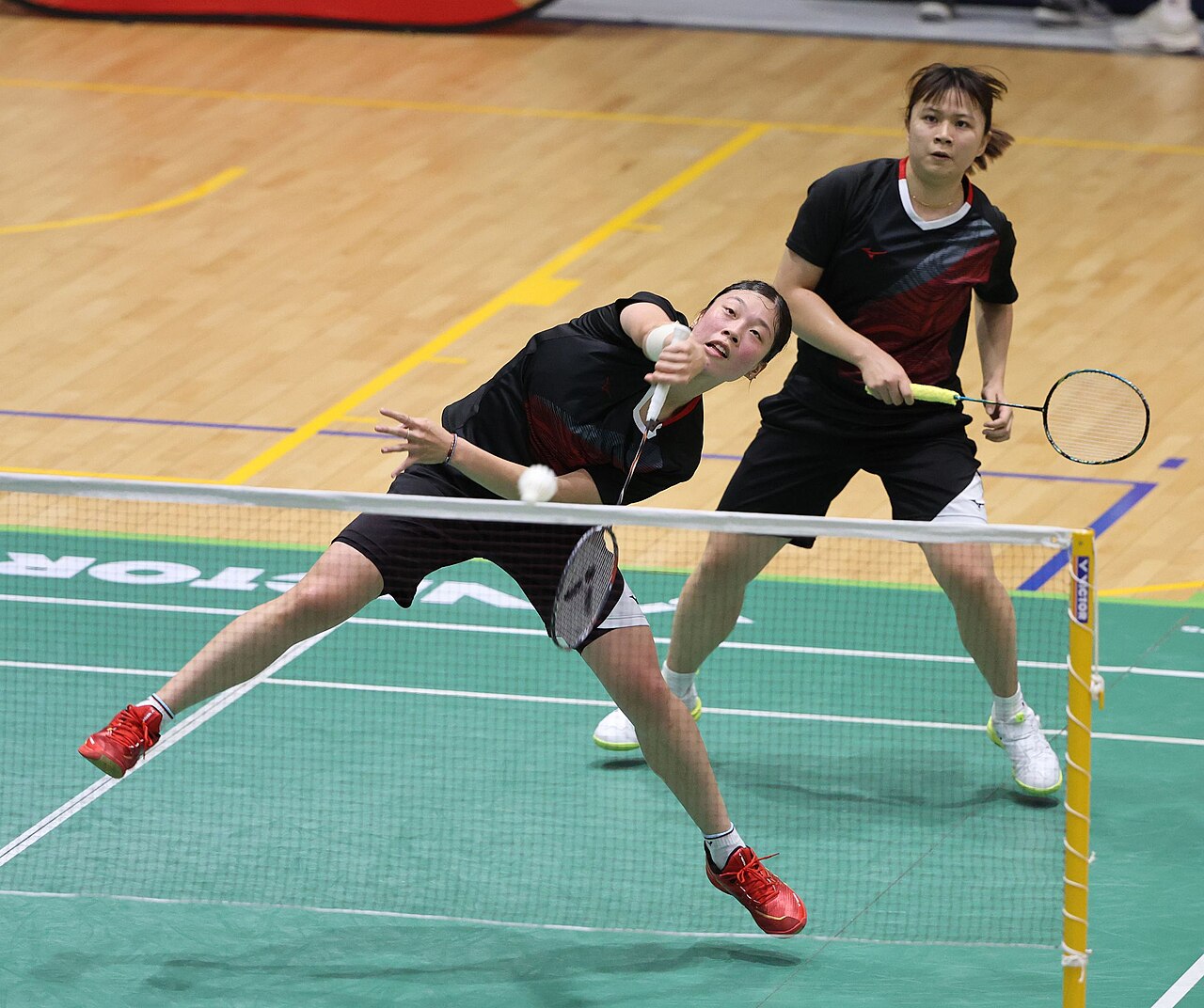Two badminton partners swing at the birdie in a doubles final.