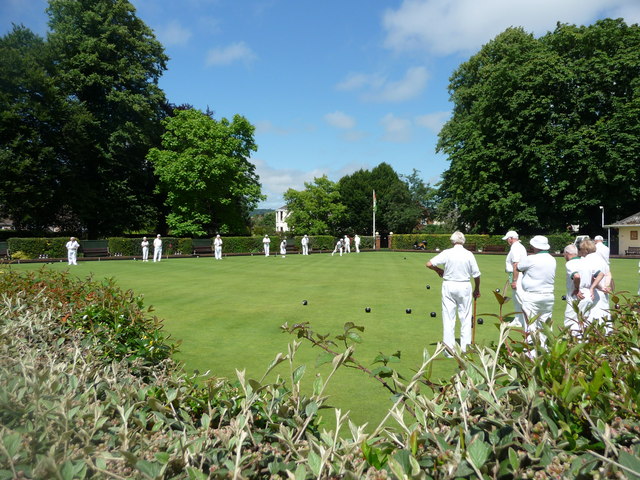 Players roll balls across a flat green lawn in a bowling game.