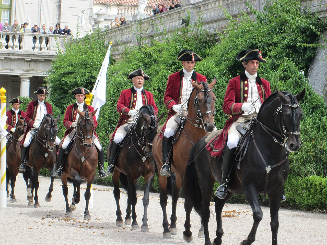 Riders on beautiful horses perform in a royal palace garden.