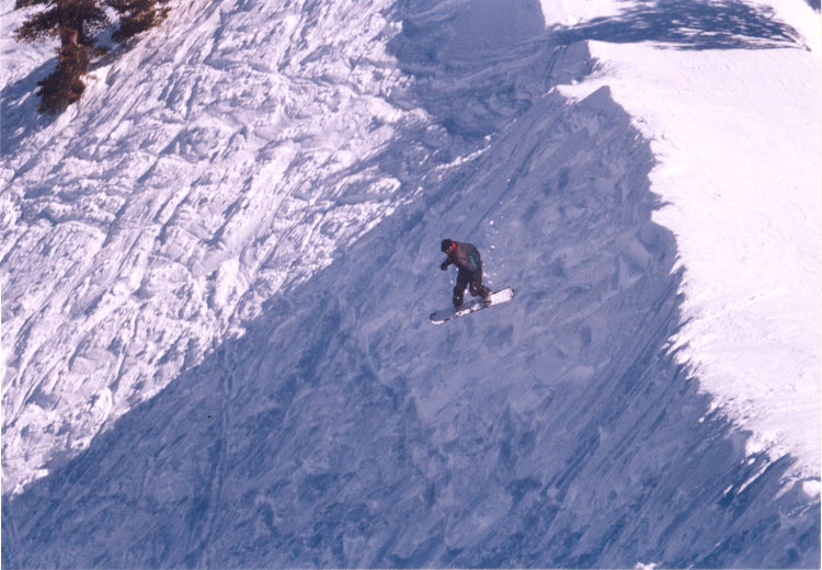 A snowboarder carves a big curve across the snowy mountain.