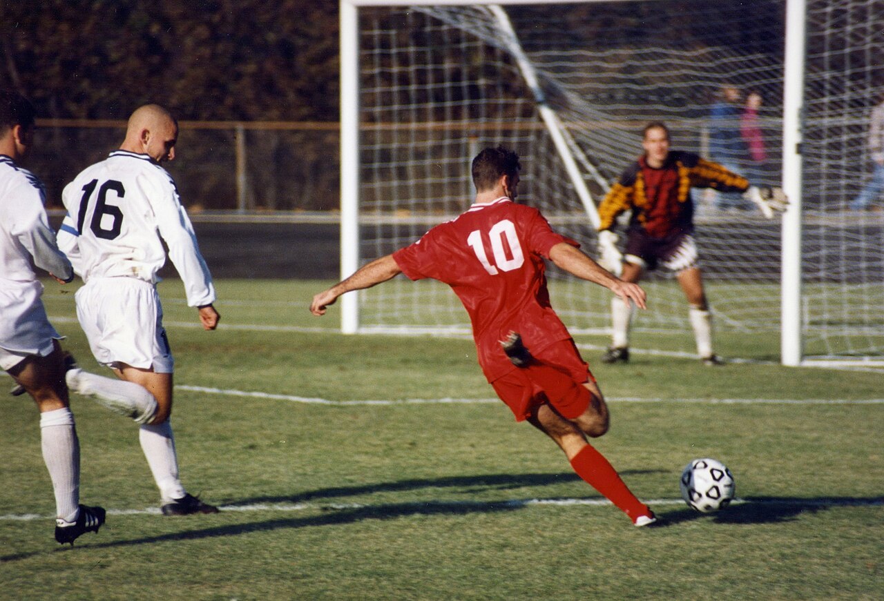 A soccer player races past two defenders and gets ready to shoot.